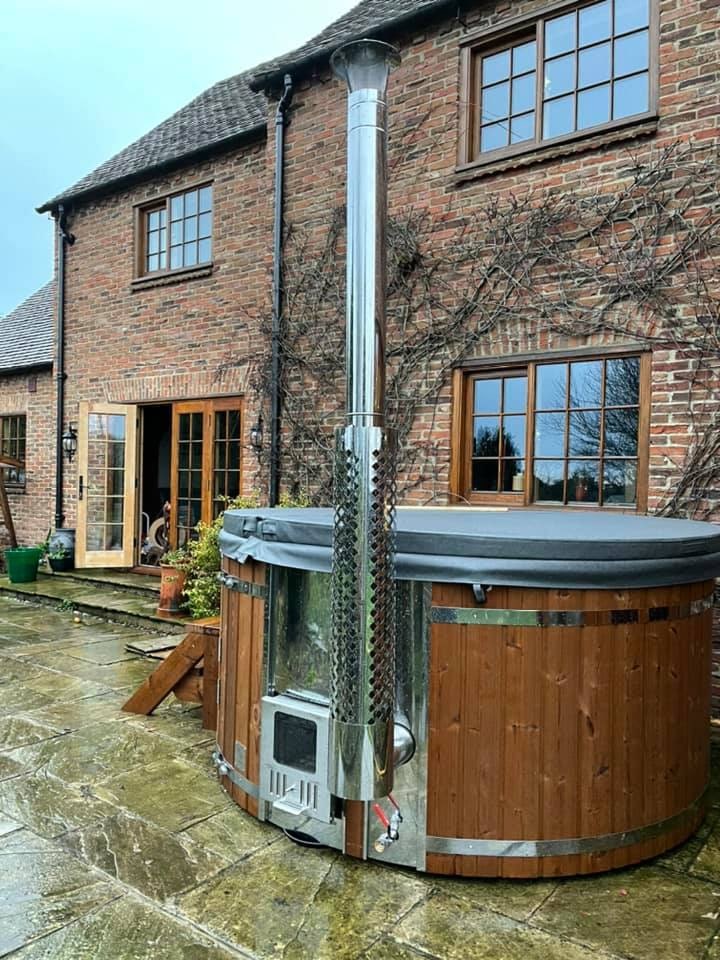 Gardenvity wood fired hot tub on stone patio beside traditional brick house in the UK.