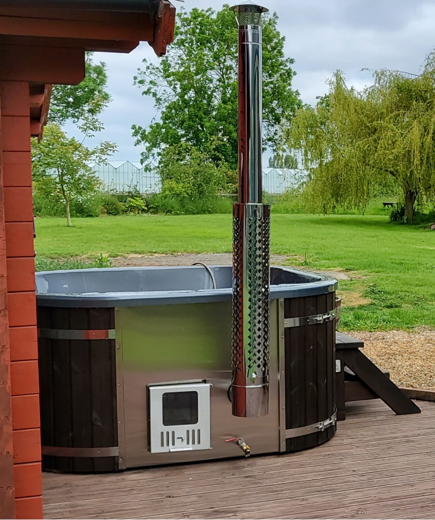 Outdoor view of wooden hot tub with metal stove, stainless steel chimney, and wooden steps on wooden deck