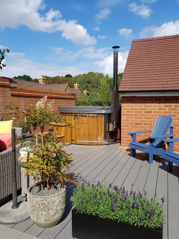 Outdoor patio scene with wooden hot tub, blue Adirondack chair, potted plants, and clear sky background