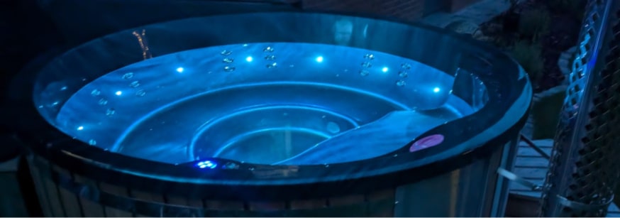 Nighttime view of a round hot tub illuminated by blue LED lights with water jets visible inside
