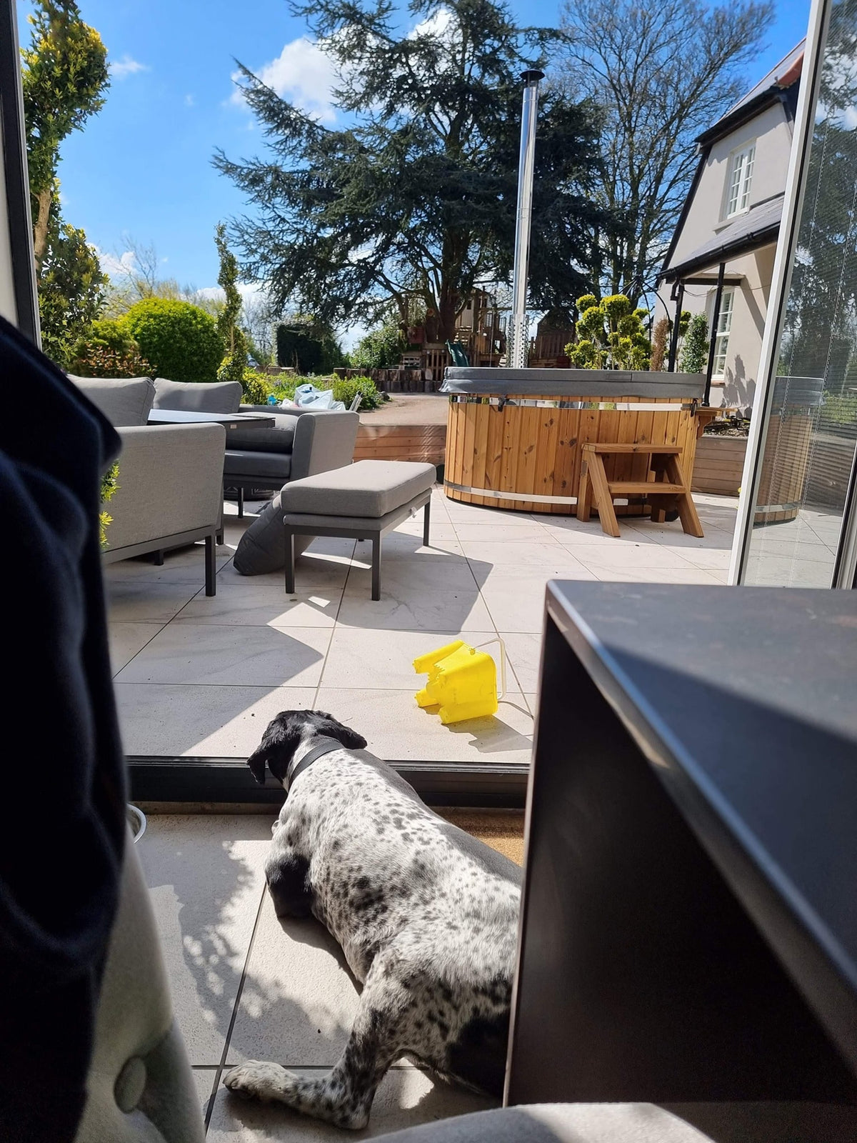Gardenvity wood fired hot tub on a modern patio with outdoor furniture and dog in view.