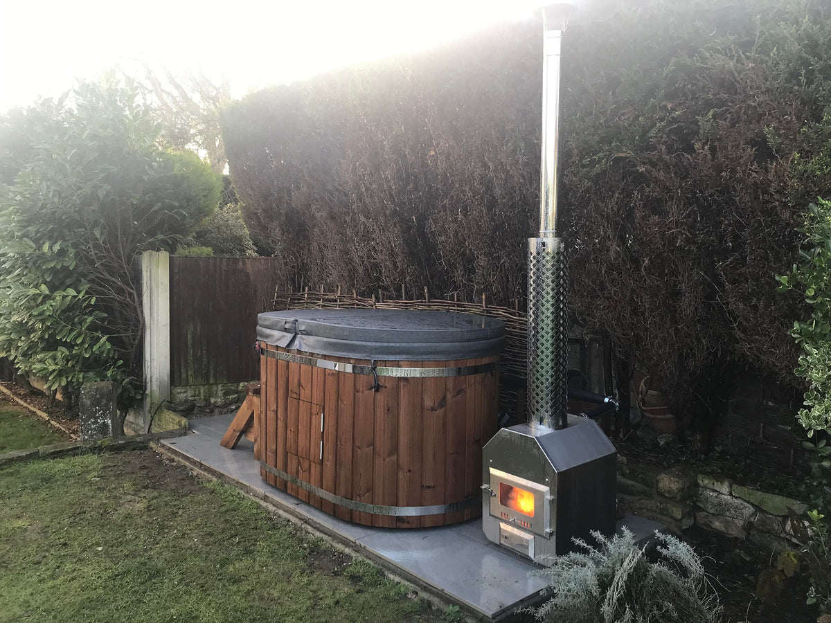Outdoor view of a wood fired hot tub with insulated cover and stainless steel stove in a garden setting