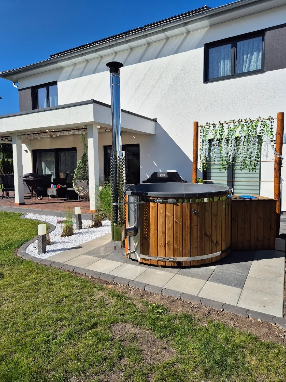 Gardenvity wood fired hot tub beside a modern house in a landscaped backyard.