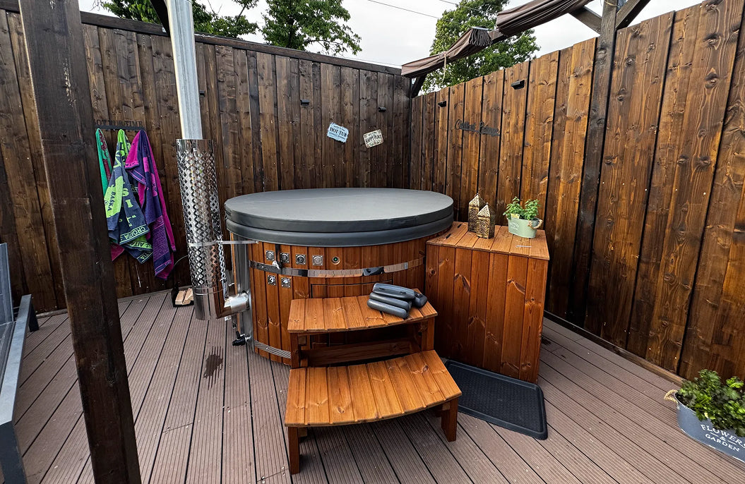 A round hot tub with a cover on the terrace, featuring a filter box, curved steps, and a stove with a chimney