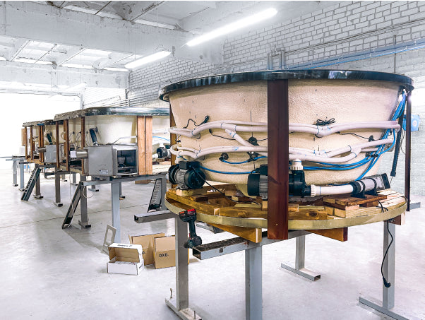 Wood-fired hot tub production line showing insulated shells, plumbing, and assembly in a European manufacturing facility