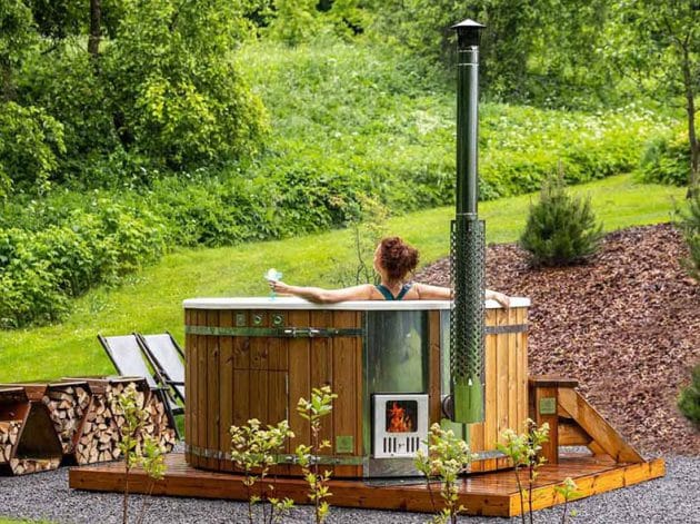 A woman relaxing in a Gardenvity wood-fired hot tub in the nature