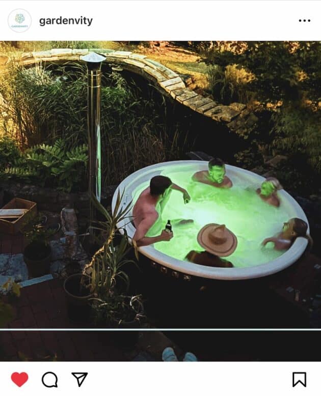 A Gardenvity wood-fired hot tub with green LED lighting in the evening, used comfortably by 5 people