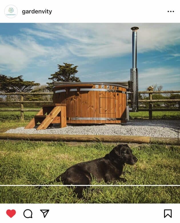 A Gardenvity wood-fired hot tub guarded by a dog