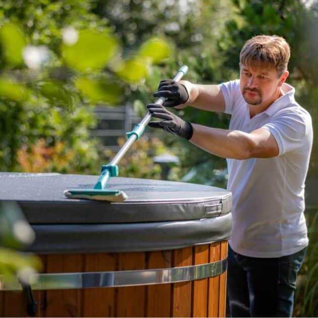 Man cleaning a wood-fired hot tub cover made of faux leather
