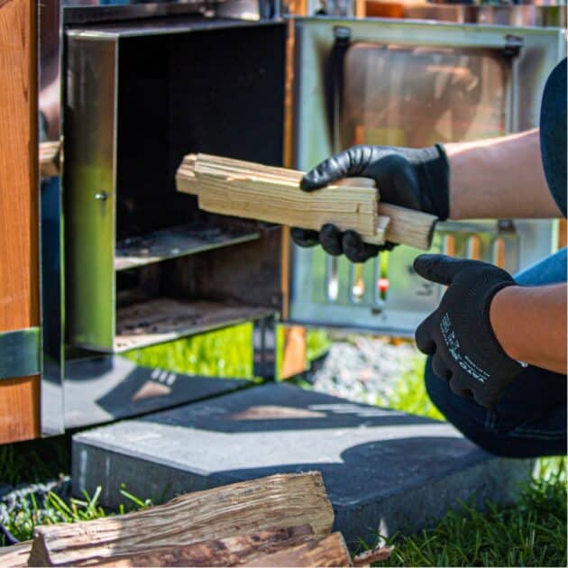 Man putting firewood to stainless steal stove of wood fired hot tub