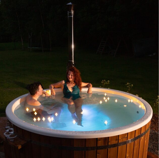Two people are relaxing in a wood-fired hot tub with multicolored points of light at night